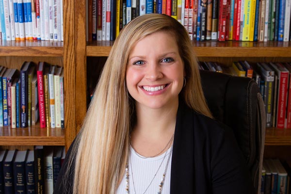 Laura sitting in front of a bookshelf smiling at the camera